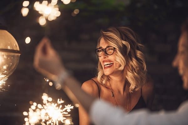 Beautiful blonde woman with style hair and glasses laughing at a holiday celebration with sparklers in the foreground